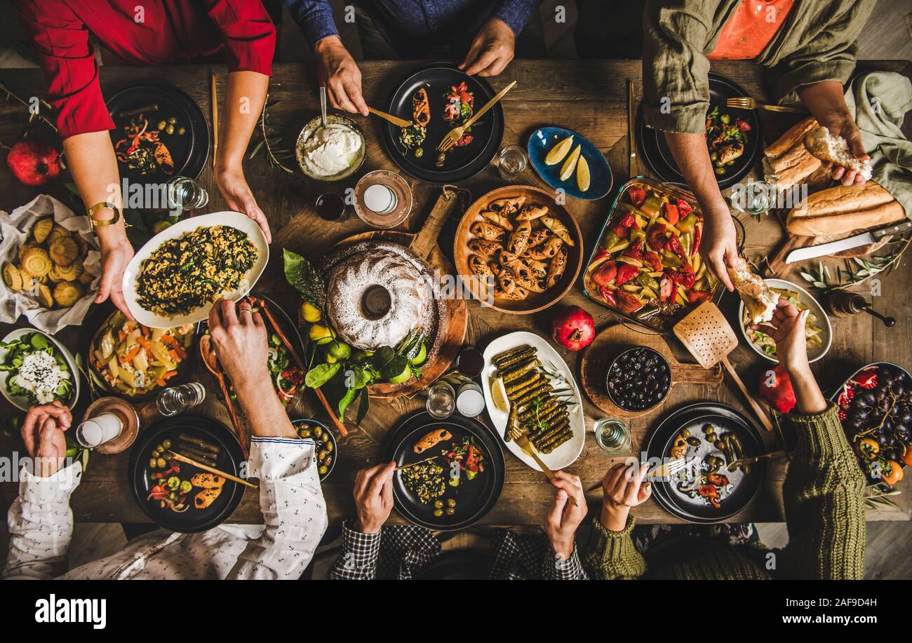 Traditional Turkish celebration dinner. Flat-lay of people feasting at table full of Turkish salads, cooked vegetables, meze starters, pastries and ra Stock Photo