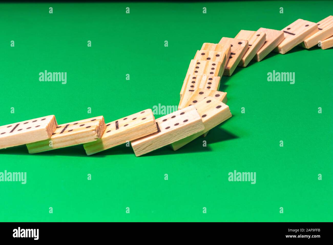 A curved line of dominoes in a domino show has been toppled, with the wooden game pieces cascading across a green surface and lying on top of each oth Stock Photo