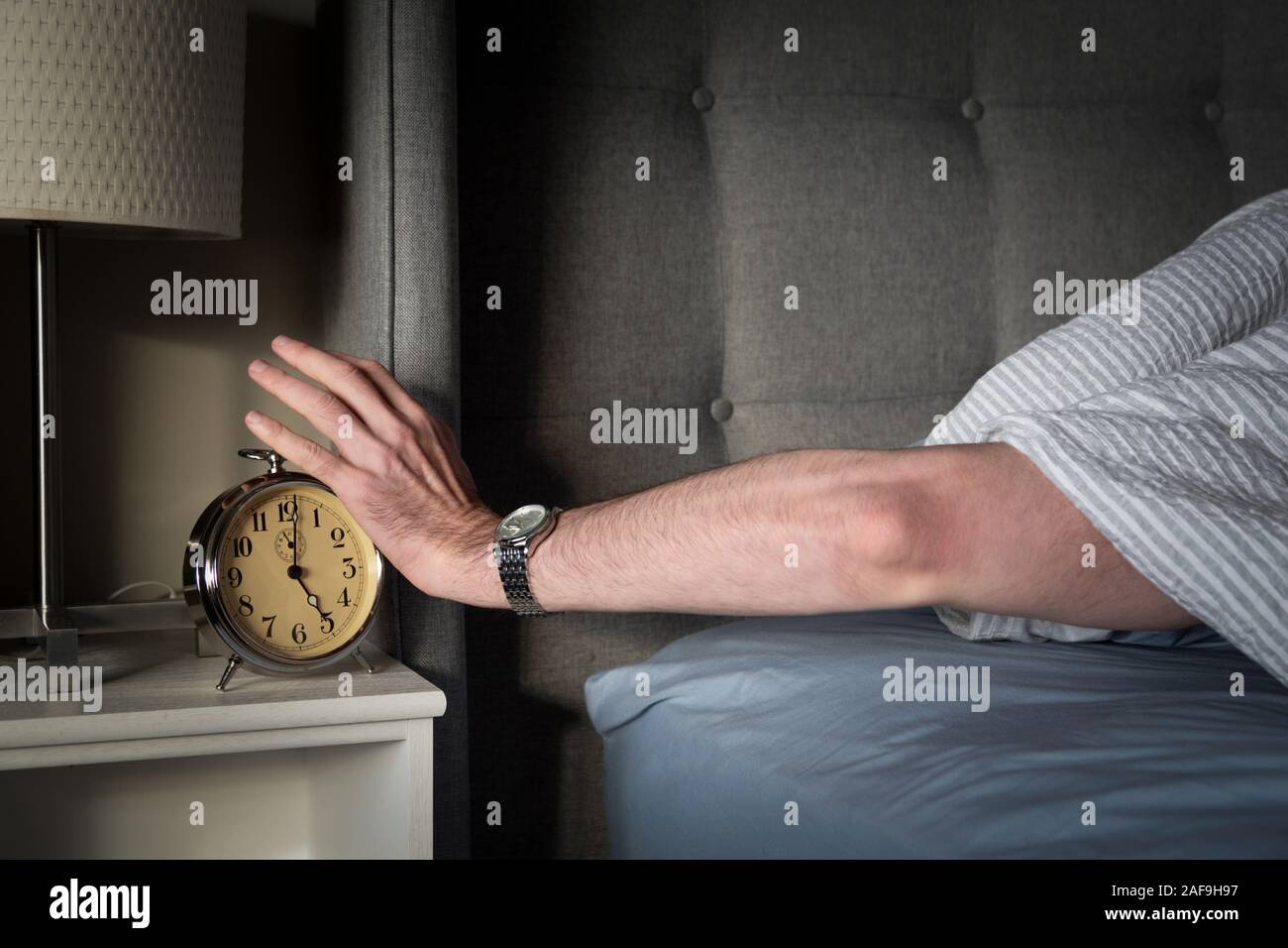 Arm reaching out from under blanket to silence an alarm clock. Stock Photo