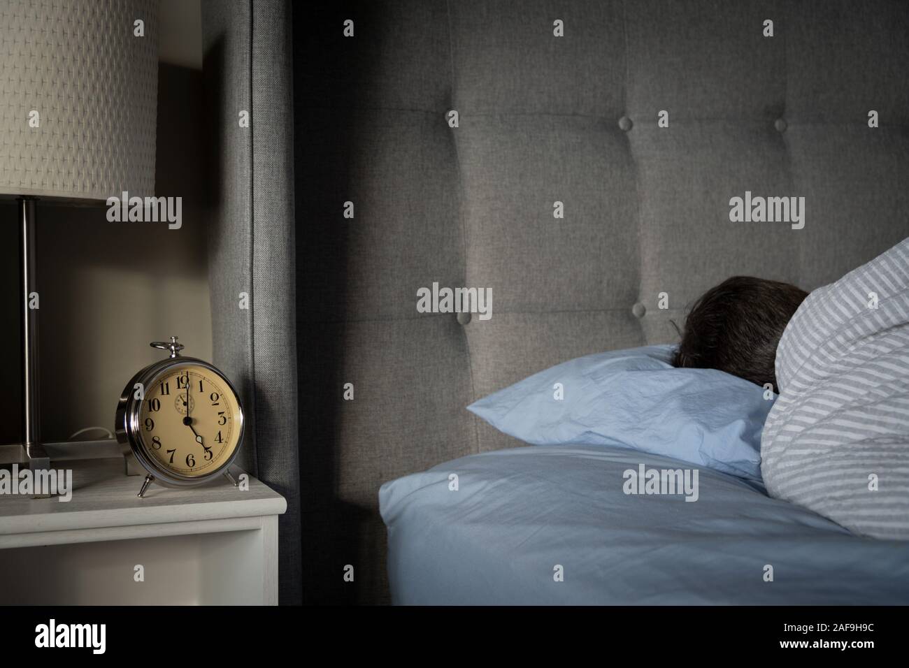 Person sleeping in bed with alarm clock on night stand. Stock Photo