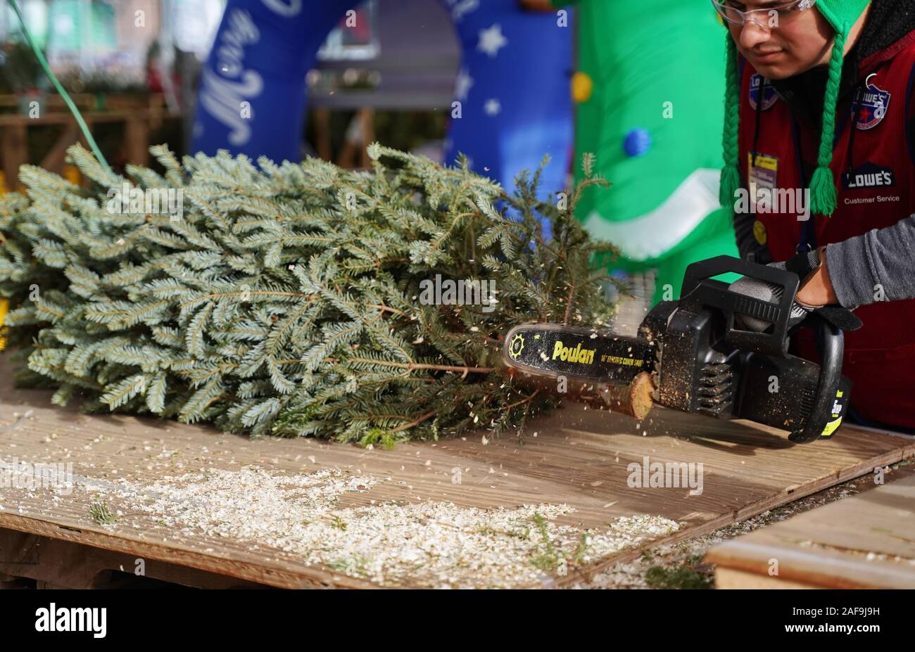 Cromwell, CT USA. Dec 2019. Electric chainsaw in action during the Christmas holidays as home improvement store employee trims tree for waiting custom Stock Photo