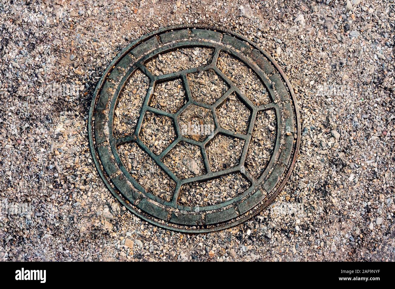 Closeup of decorative old man hole cover in Ceret, France, surrounded by gravel Stock Photo