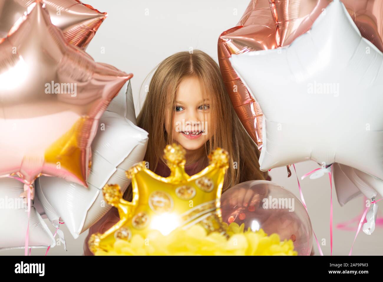 Little girl playing with balloons. Portrait of little girl playing with air balloons. Happy little girl holding colorful balloons.Smiling kid. Stock Photo