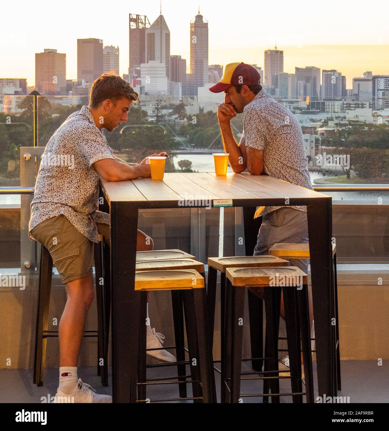 Two Caucasian males drinking beer at alfresco bar at dusk at Optus Stadium Perth Western Australia. Stock Photo
