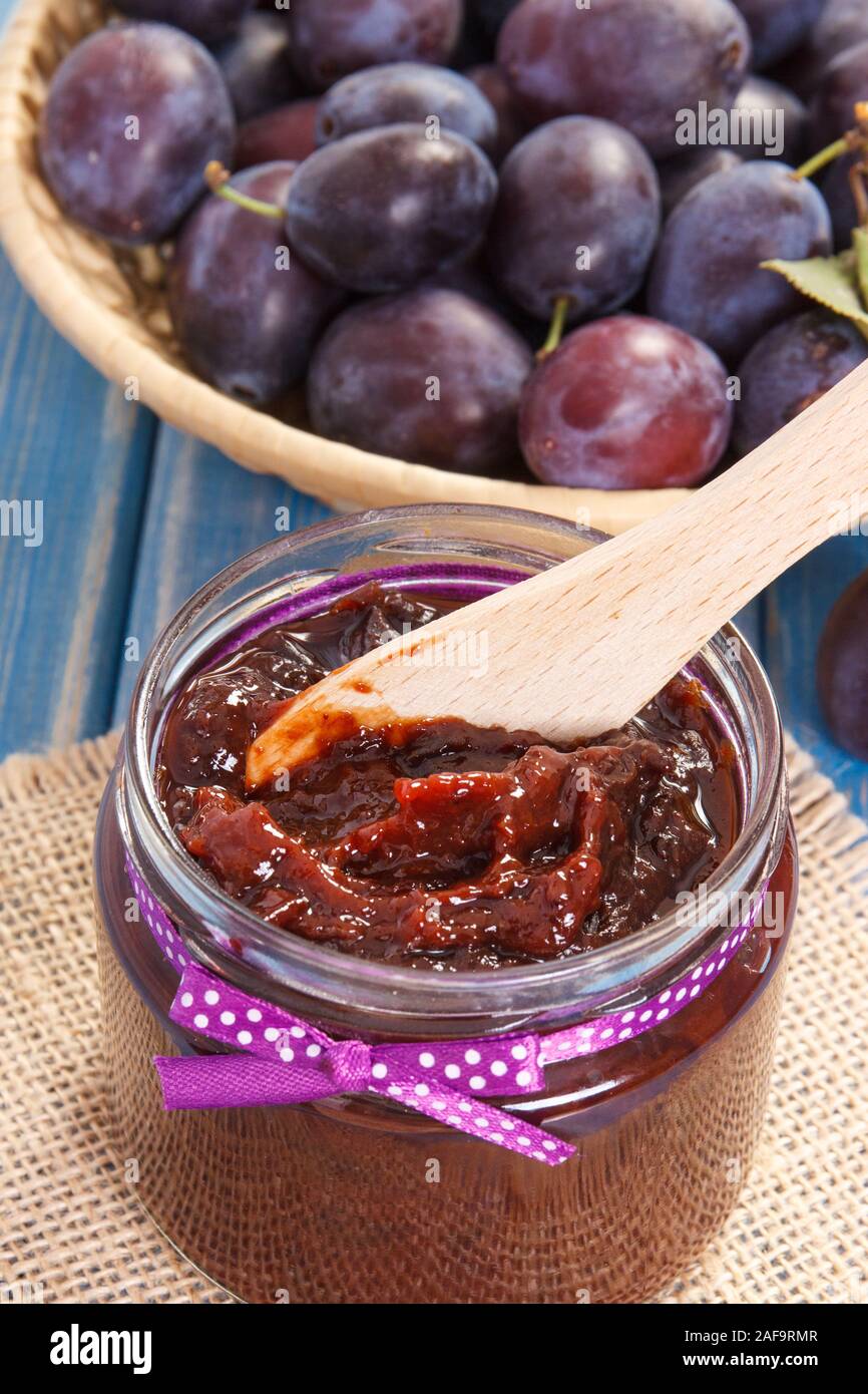Wooden knife and homemade plum marmalade or jam in glass jar, concept of healthy sweet snack or dessert Stock Photo