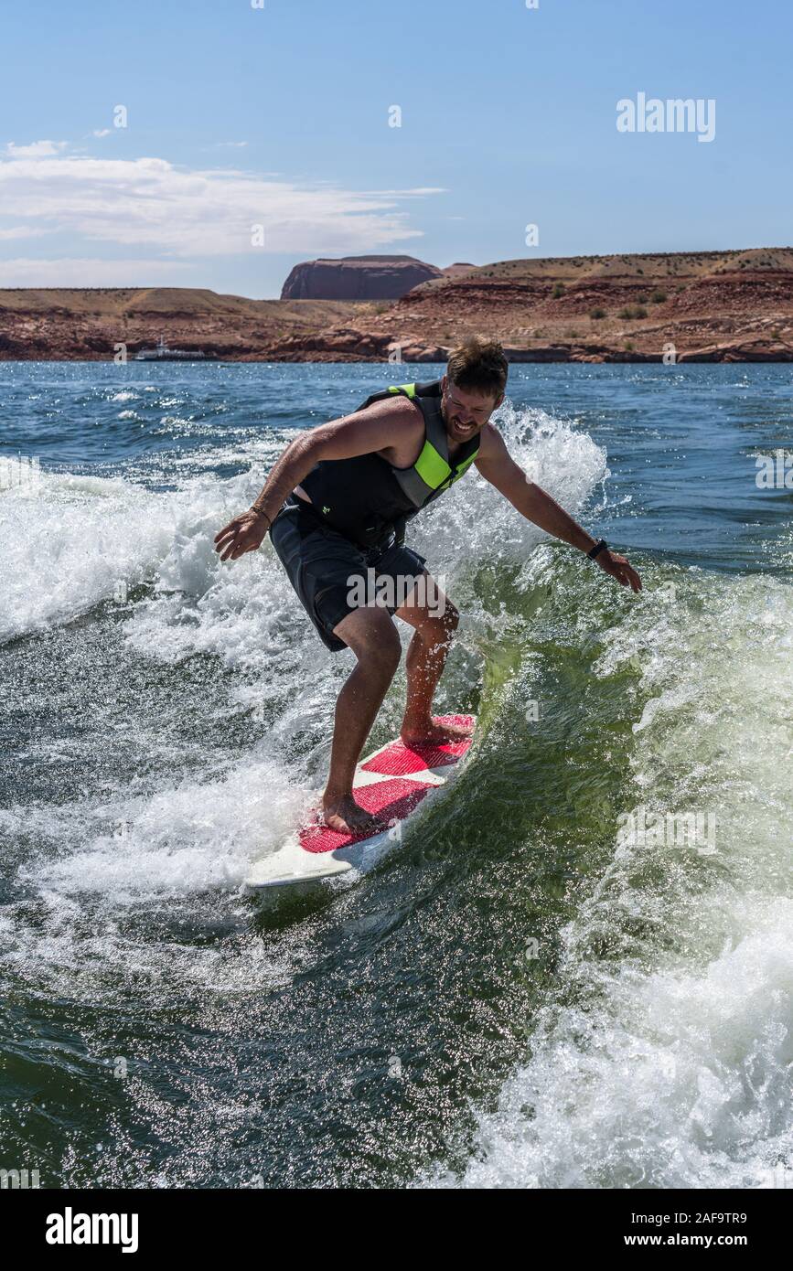 A young man wake surfing behind a boat on Lake Powell in the Glen