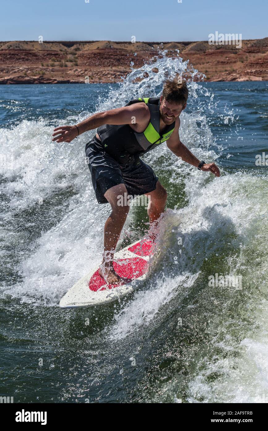 A young man wake surfing behind a boat on Lake Powell in the Glen