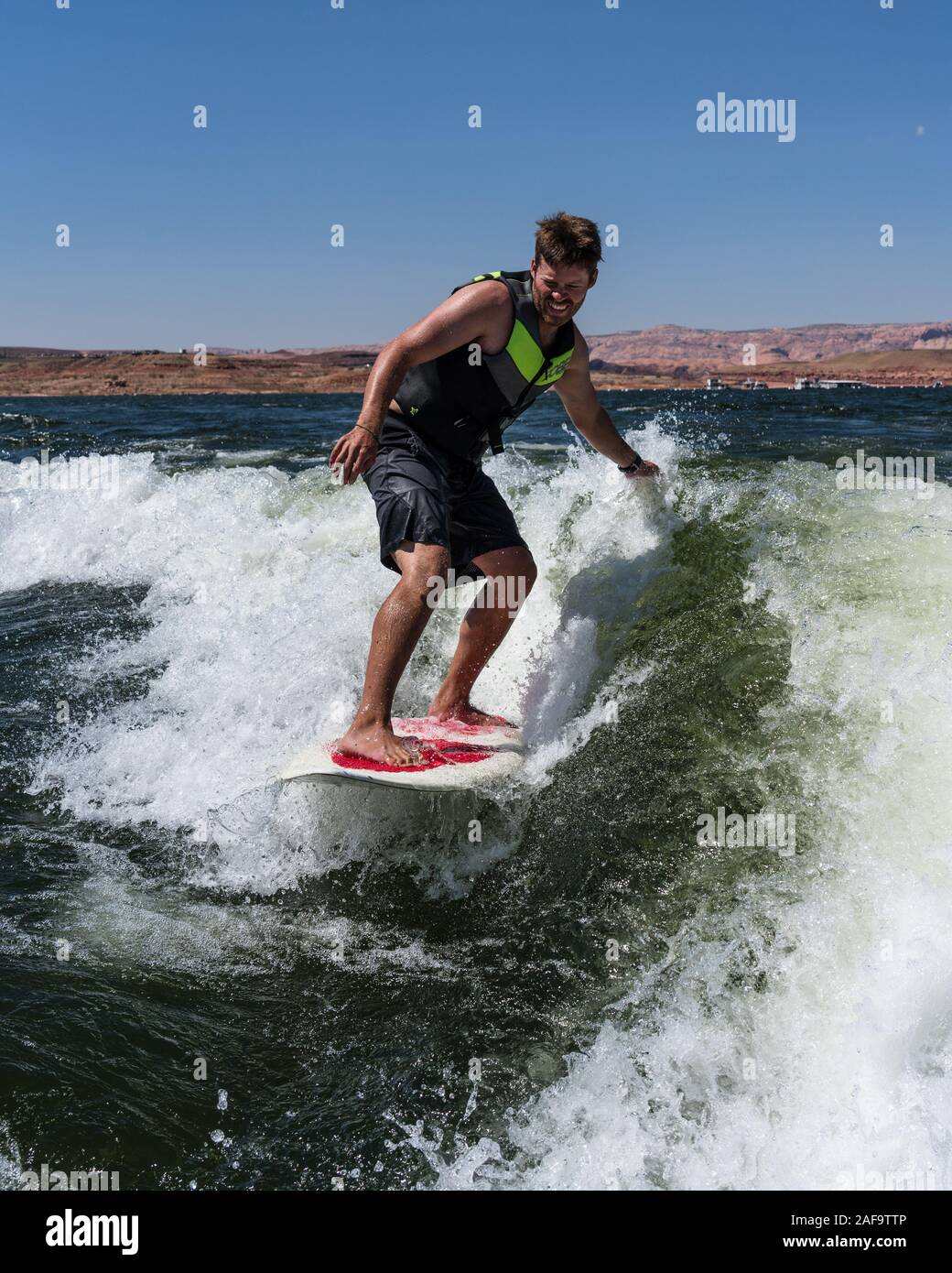 A young man wake surfing behind a boat on Lake Powell in the Glen