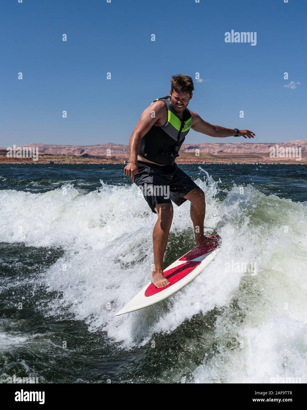 A young man wake surfing behind a boat on Lake Powell in the Glen