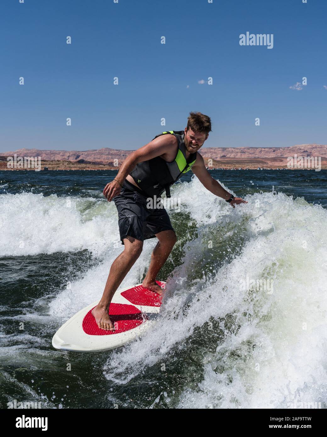 A young man wake surfing behind a boat on Lake Powell in the Glen