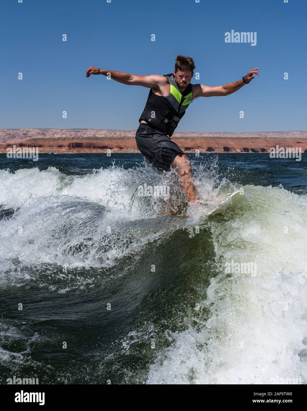 A young man wake surfing behind a boat on Lake Powell in the Glen