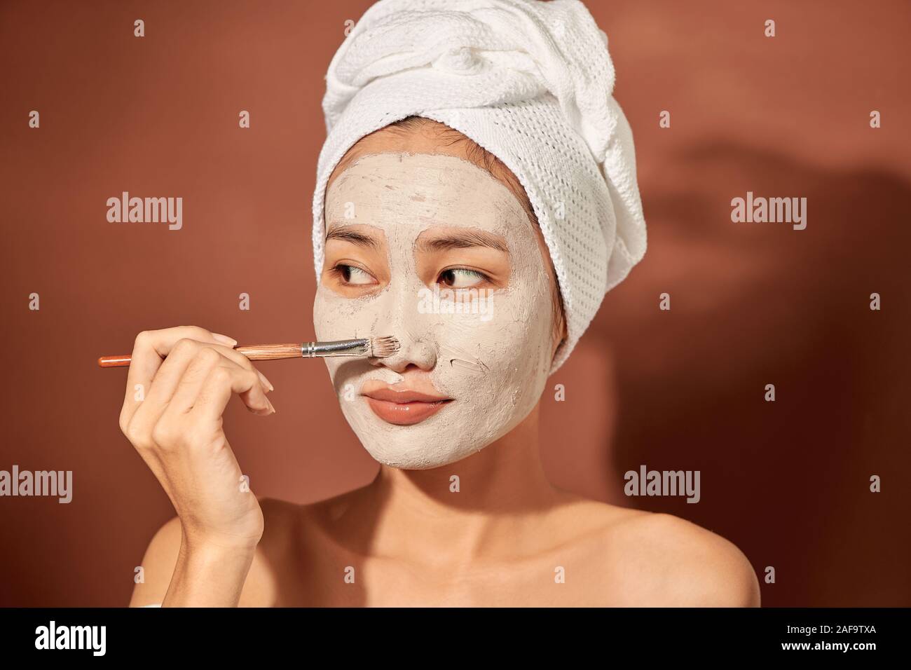 Attracitve young Asian woman applying clay mask on her facee. Spa and wellness, skin care product concept. Stock Photo