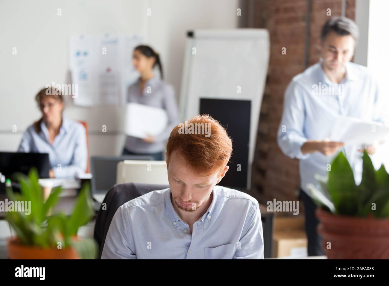 Employees working in shared office focus on busy redhead man Stock Photo
