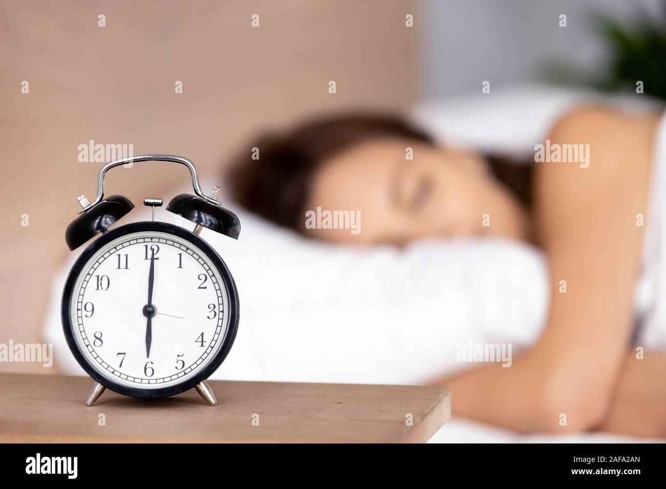 Alarm clock on bedside table with woman sleeping on background Stock Photo