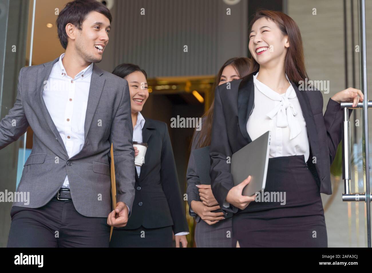 Asian business people walking to go out office building. Young businessman and businesswoman talking and Open the office door. Stock Photo