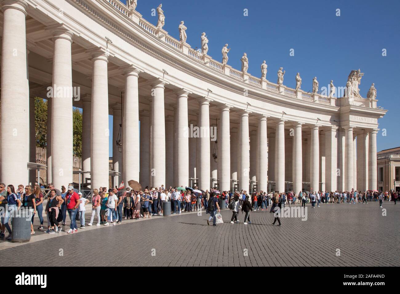 A line of visitors queue by Bernini's colonnade in St Peter's Square, waiting to get into St. Peter's Basilica, Rome Stock Photo