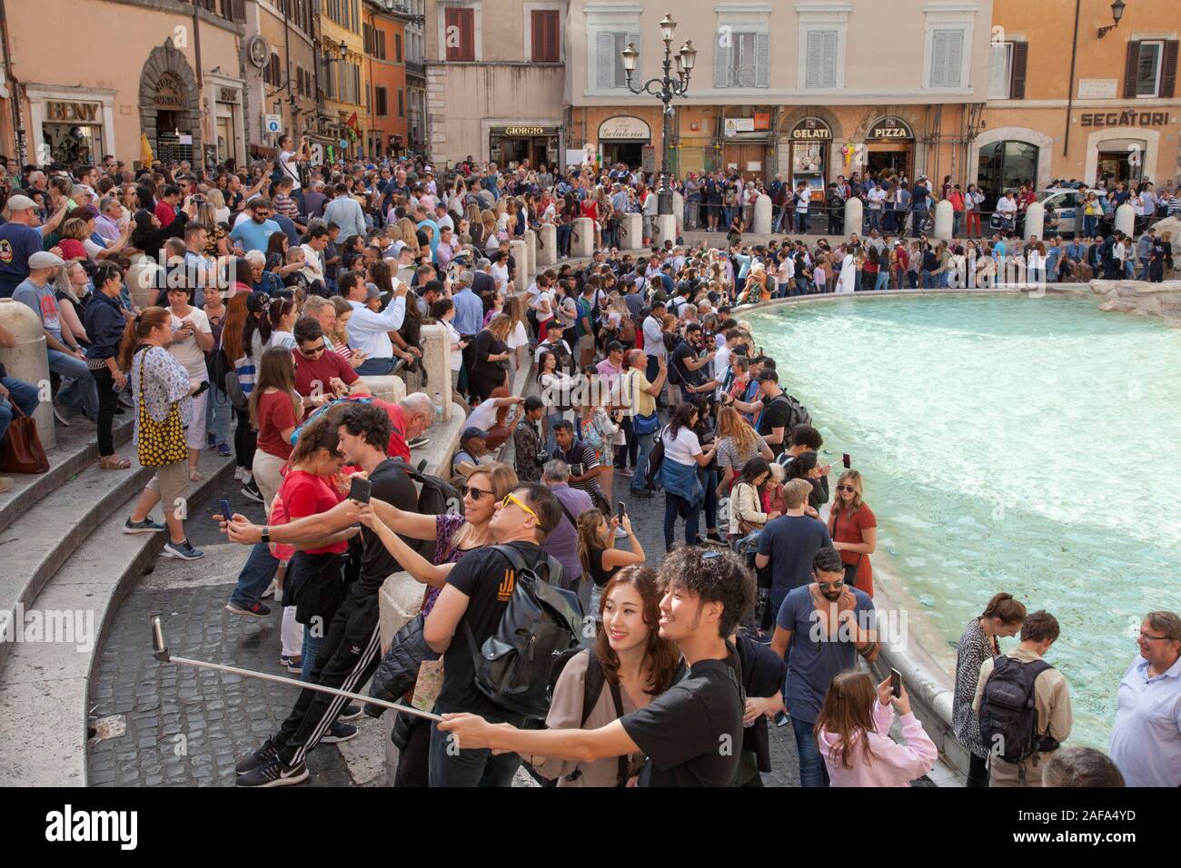 Huge crowds at the Trevi Fountain in Rome take selfies and throw coins into the fountain for luck. Security now stop people from sitting Stock Photo