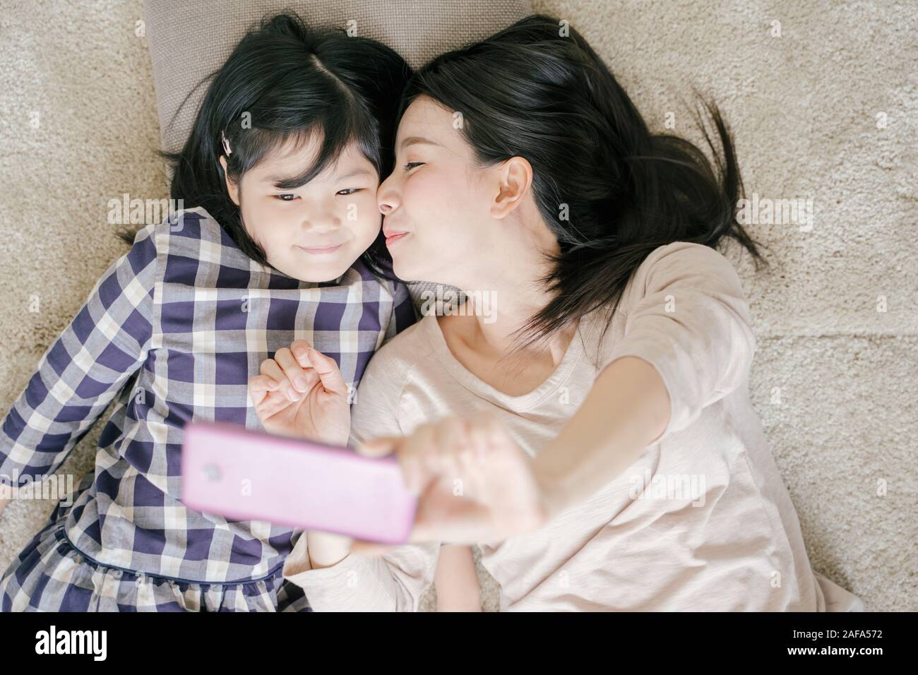 Mother is selfie with her little daughter using a smart phone camera while kissing daughter cheek Stock Photo
