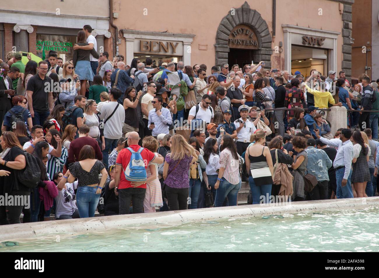 Huge crowds at the Trevi Fountain in Rome take selfies and throw coins into the fountain for luck. Security now stop people from sitting Stock Photo