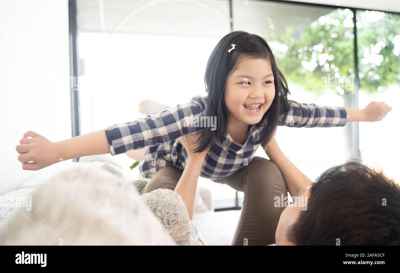 Happy little girl daughter playing with father while ride dad back and dad lying on the bed at home Stock Photo