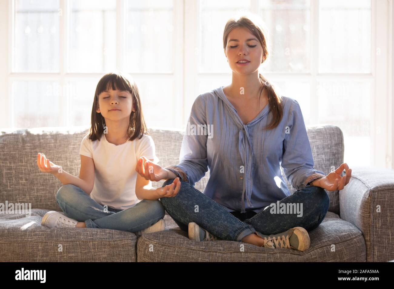 Calm smiling mother with cute little daughter doing yoga exercise Stock Photo