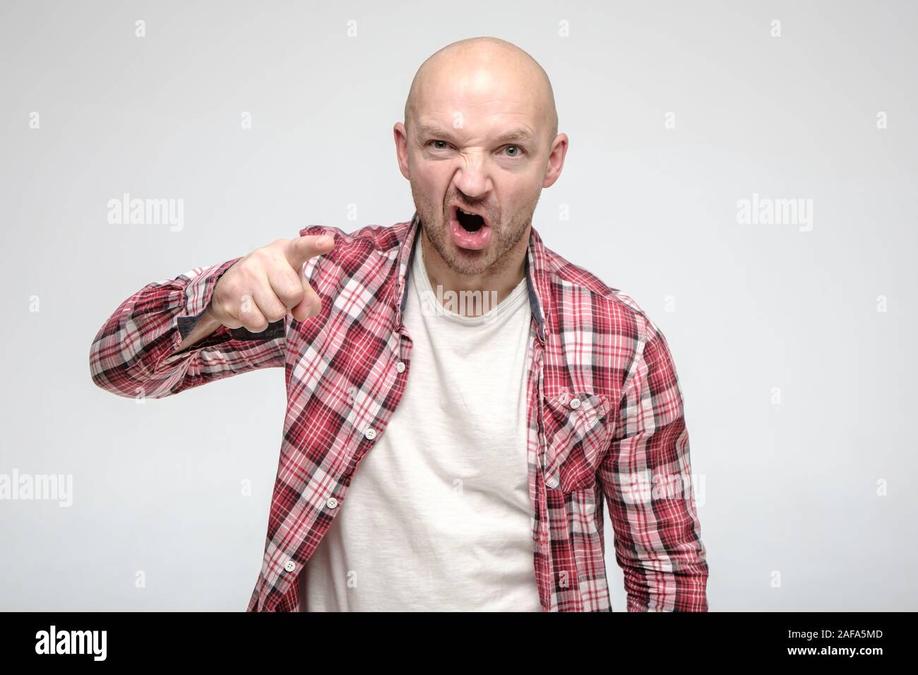 Angry, an aggressive bald man with stubble points index finger at someone and accusing, looking at the camera. Stock Photo
