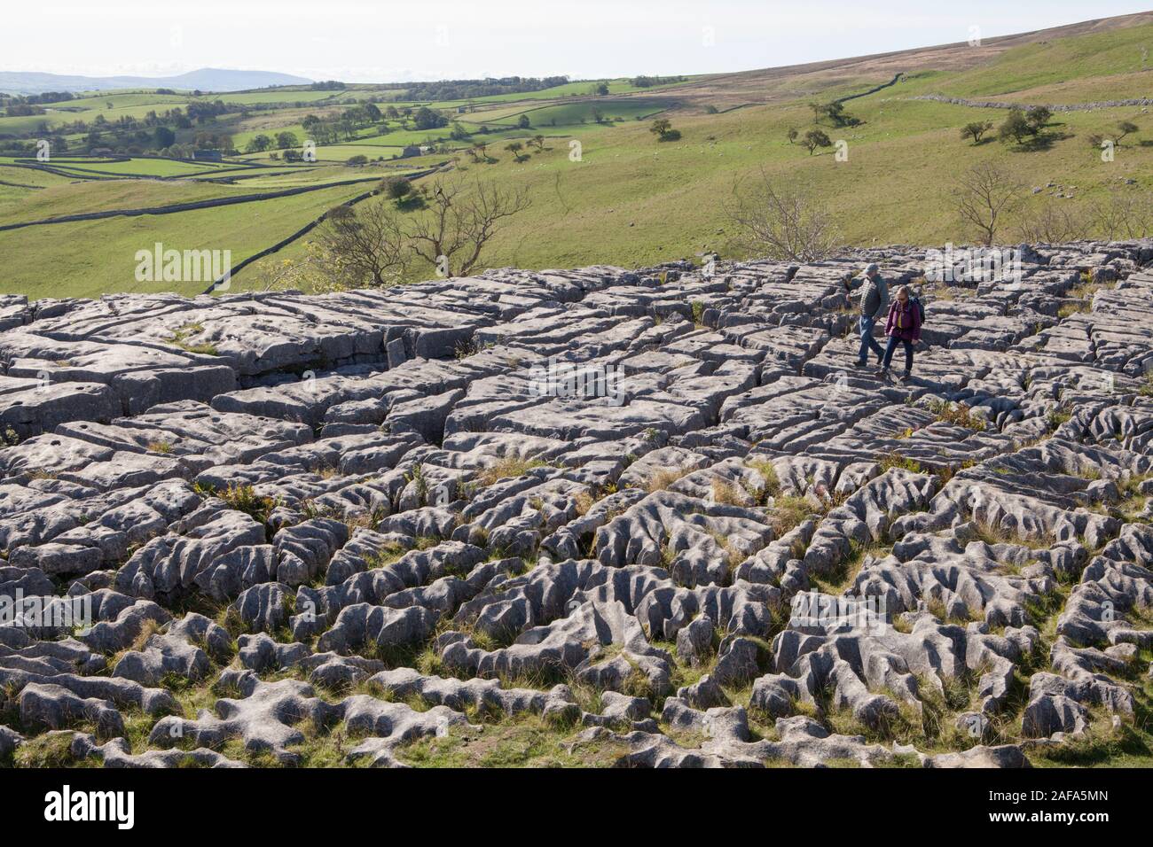 Two adults walk across the limsestone pavement at the top of Malham Cove in the Yorkshire Dales Stock Photo