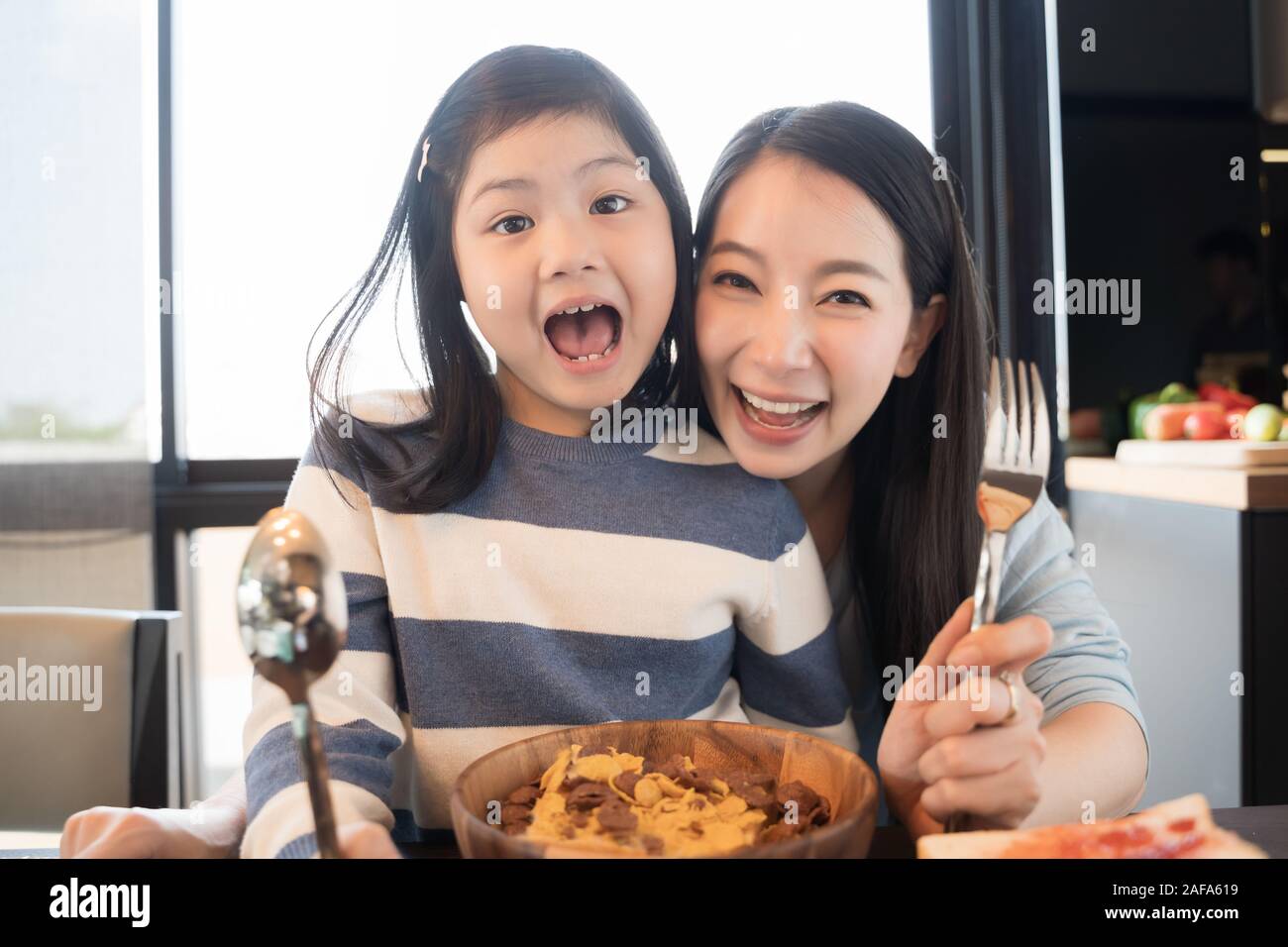 mom and daughter eating Cereals with milk having breakfast in kitchen. Stock Photo
