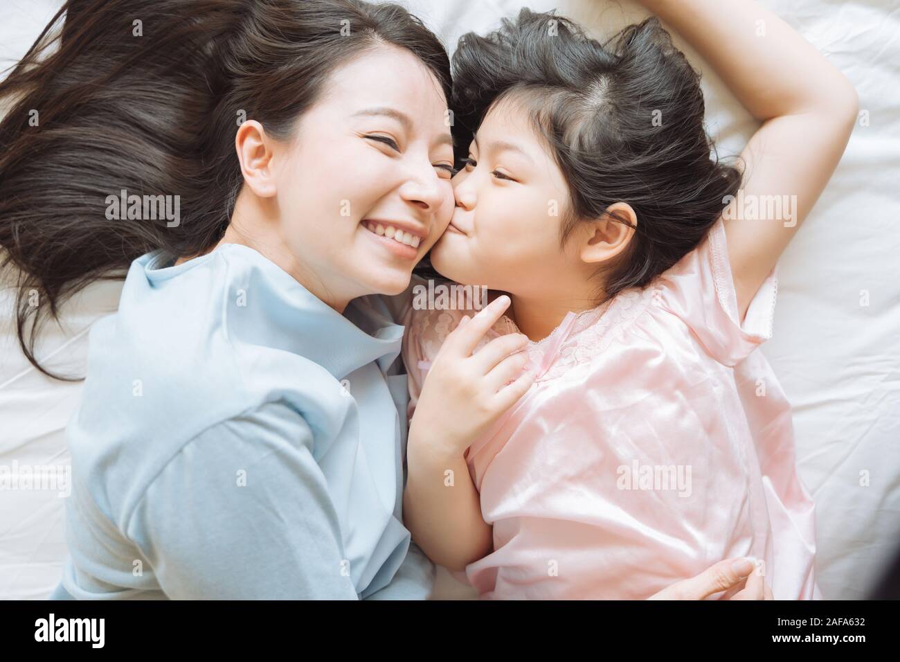 Daughter kisses her mother's cheek. and hugging in the bedroom .Happy Asian family Stock Photo