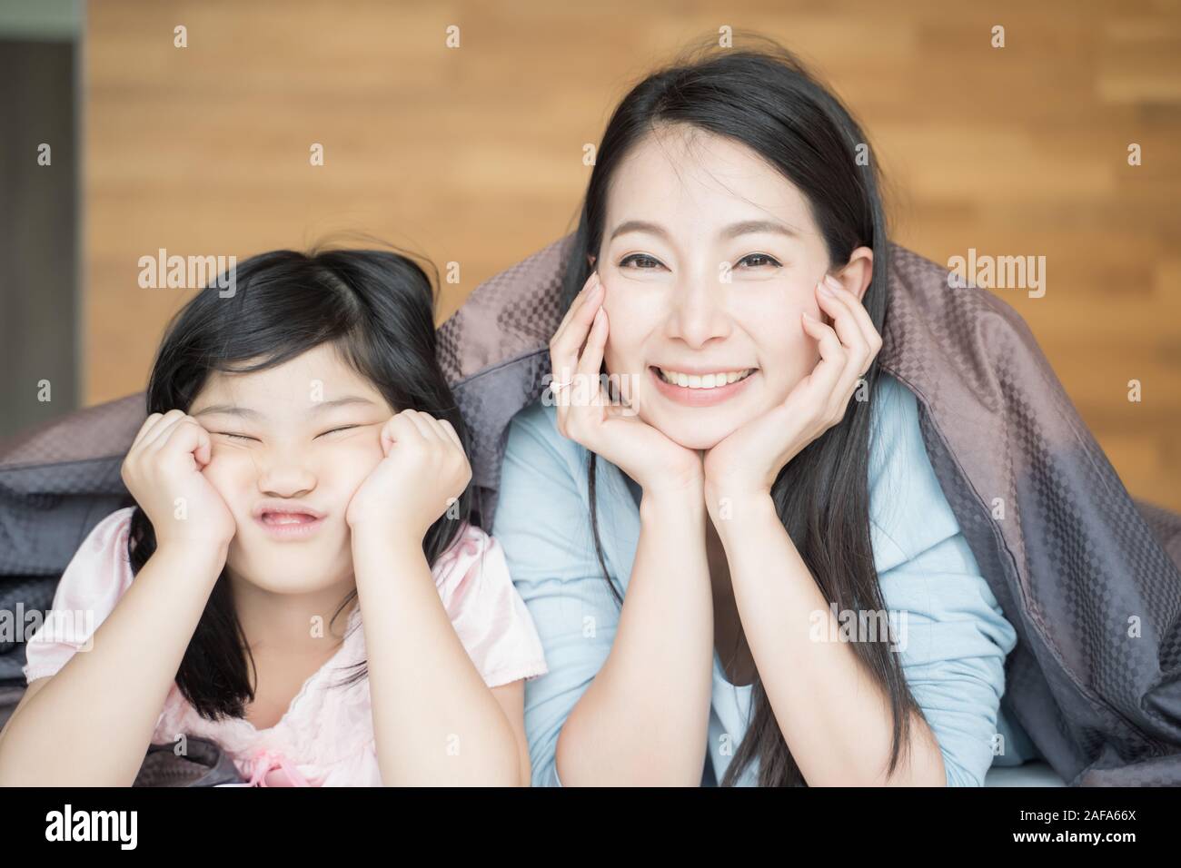 Mother and her daughter child girl playing in the bedroom and putting blanket on . Happy Asian family Stock Photo