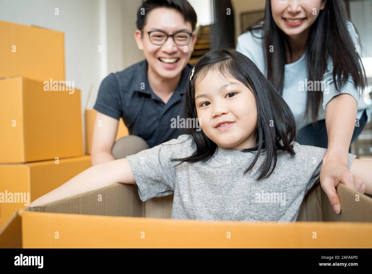 Portrait of happy Asian family moving to new house with cardboard boxes and playing cardboard box Stock Photo