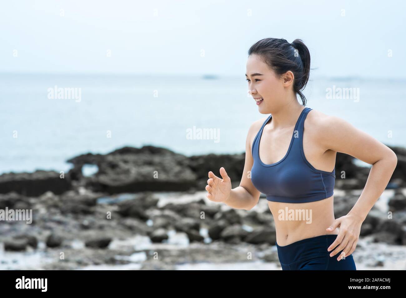 Young Asian woman running on the beach. Girl jogging workout in seaside Stock Photo