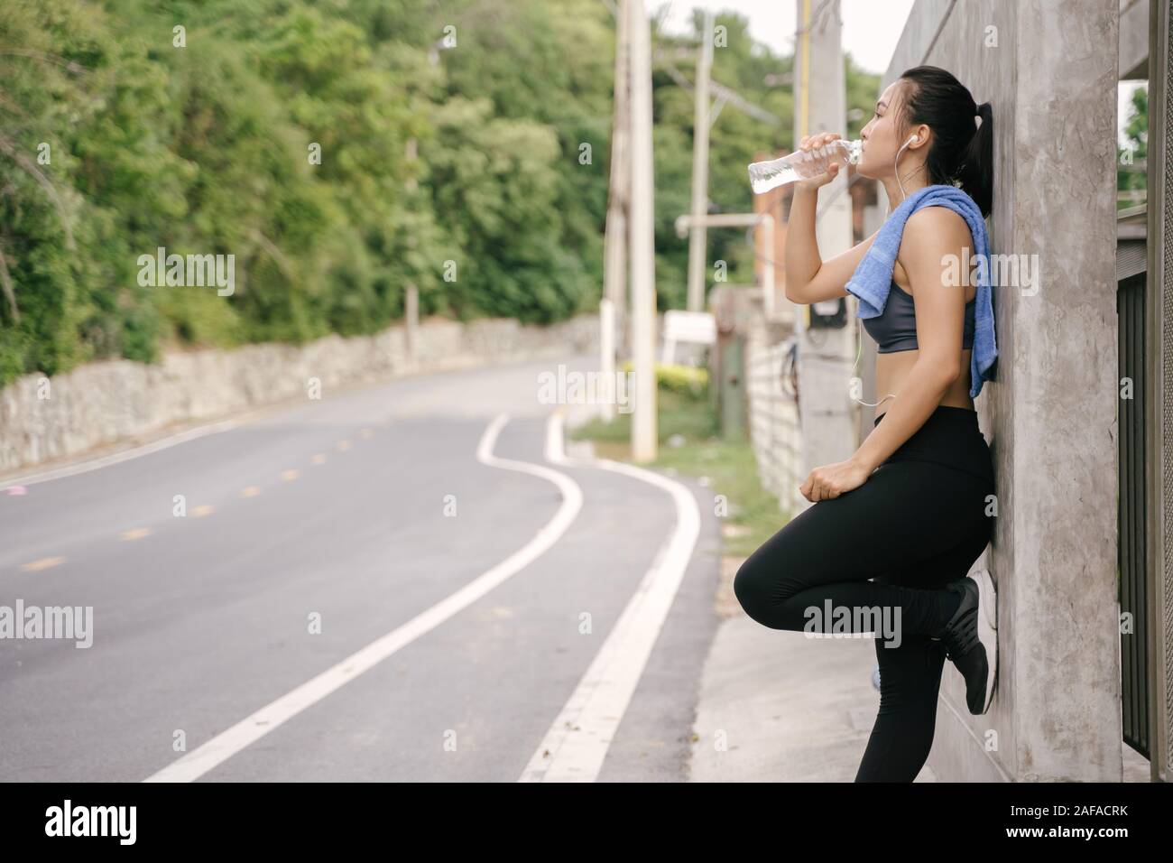 Young Asian woman runner resting after workout running and drinking water in street road. Stock Photo