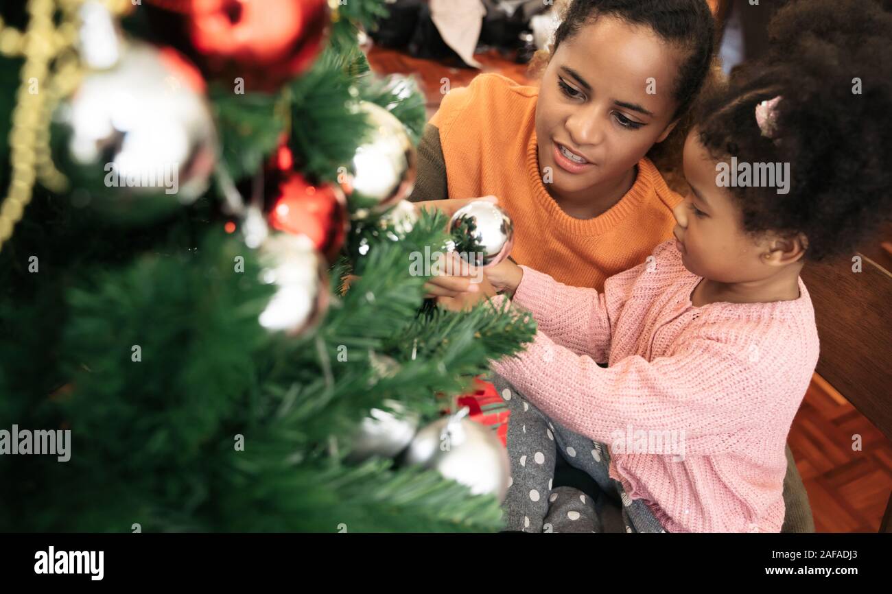 Mother and daughter african american girl decorating Christmas tree with ,arranging the christmas lights and having fun Stock Photo