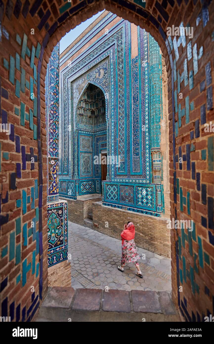 woman walks through narrow path through facades heavily decorated with blue tiles in necropolis Shah-i-Zinda, Samarqand, Uzbekistan, Central Asia Stock Photo