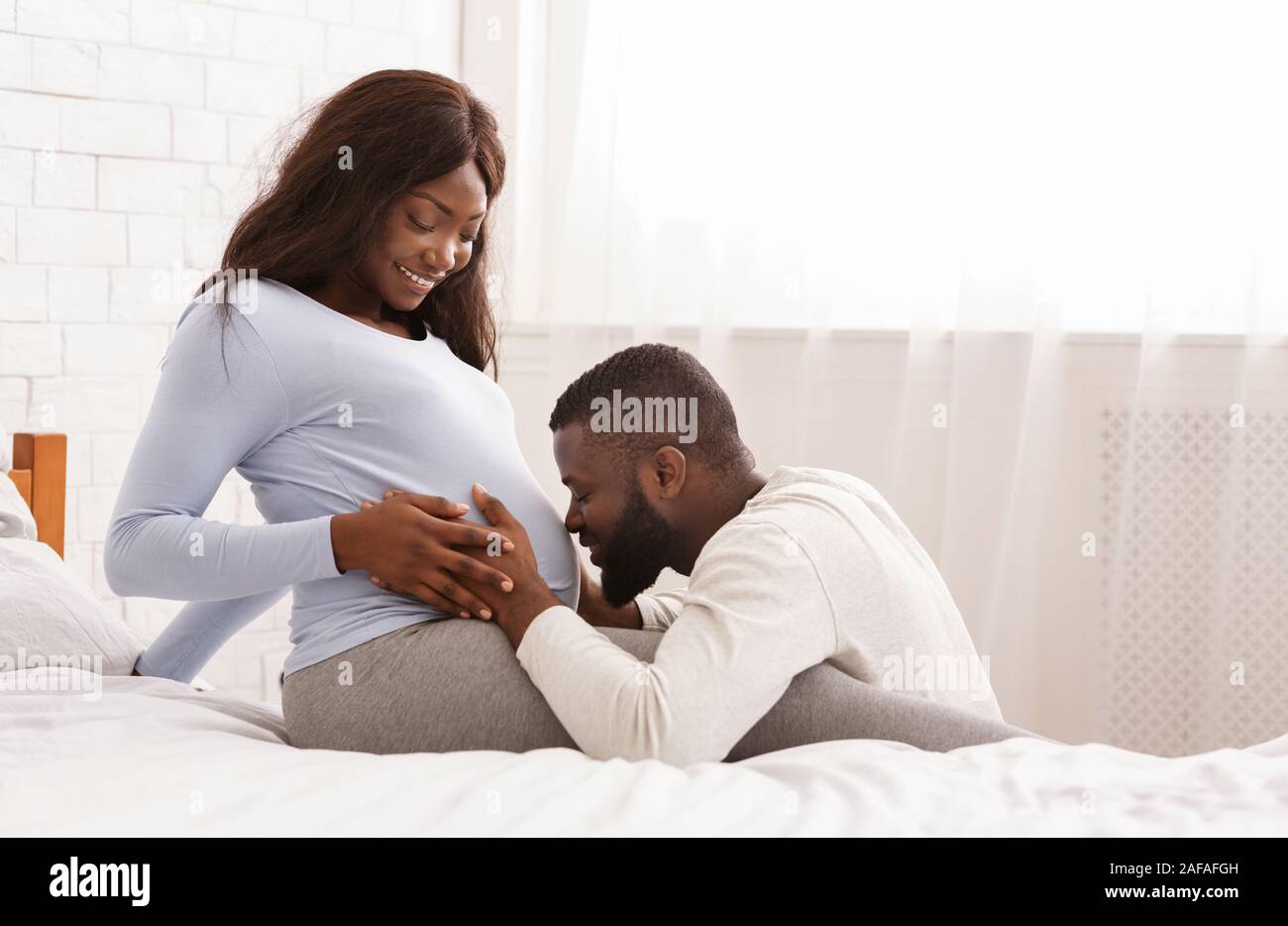 Blissful man kissing his happy pregnant wife belly Stock Photo