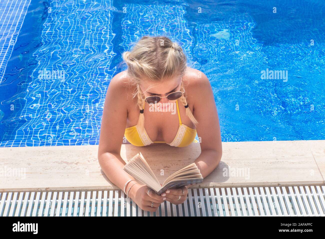Relaxing by a pool on holiday reading a book Stock Photo