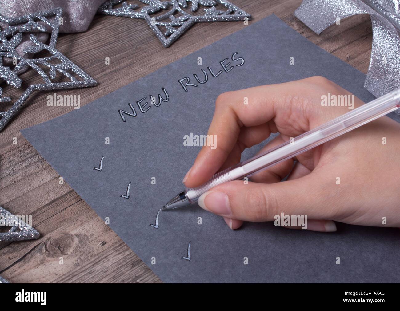 A person writes words on grey paper. New year, new rules. Motivation, plan, schedule, task, new life. Christmas, holiday. Snowflakes and Christmas toy Stock Photo