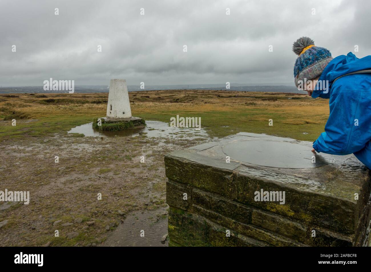Person wearing a bobble hat looking at the directional map at the trig point at the top of Baildon Moor, near Bradford in West Yorkshire Stock Photo