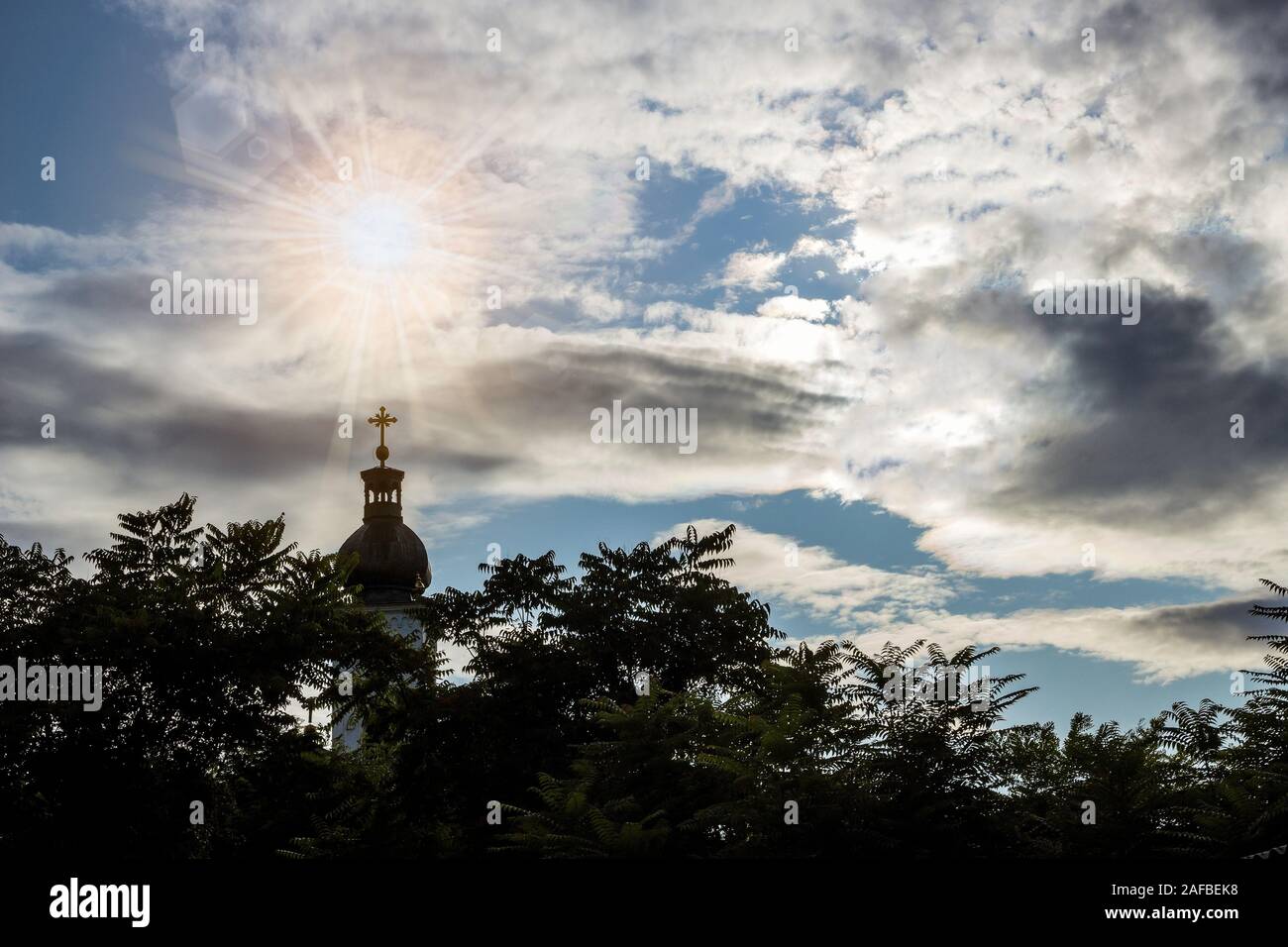 Church and trees silhouettes with sun rays during a hot summer day. Stock Photo