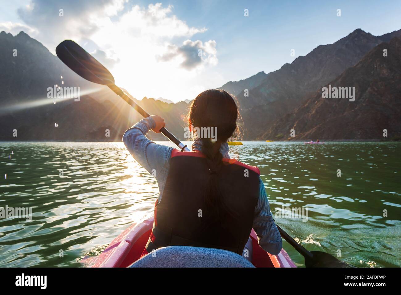 Woman kayaking in a mountain surrounded lake at sunset Stock Photo