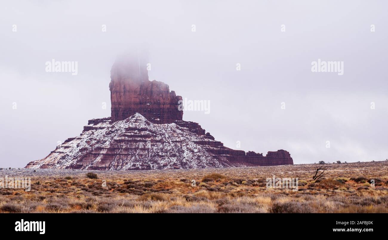 The top of the Big Chief at Monument Valley Navajo Tribal Park disappears in the low hanging clouds Stock Photo