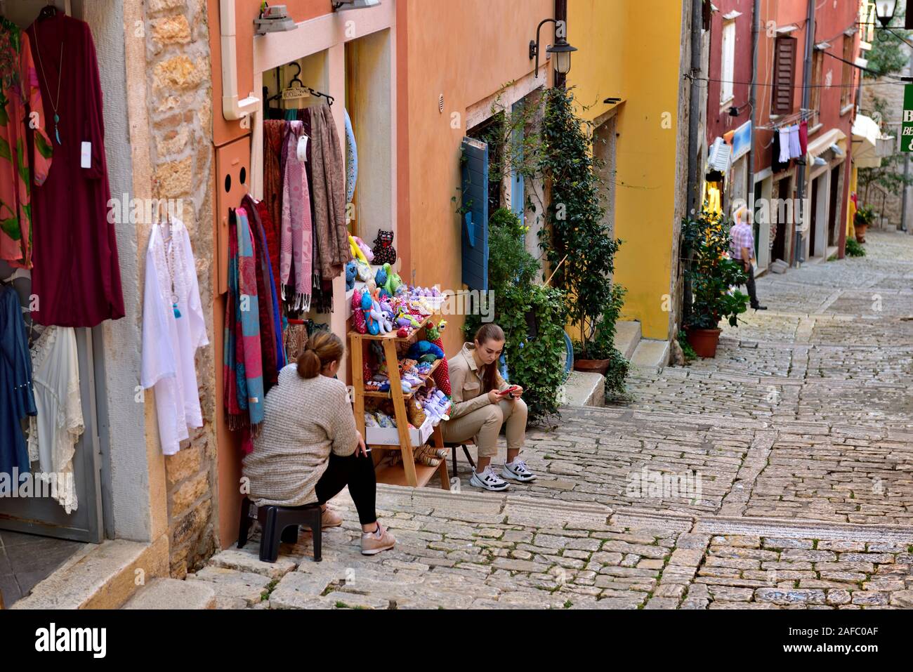 Small cobblestone pedestrian street with steps, small shops, shopkeepers relaxing outside, Rovinj, Croatia Stock Photo