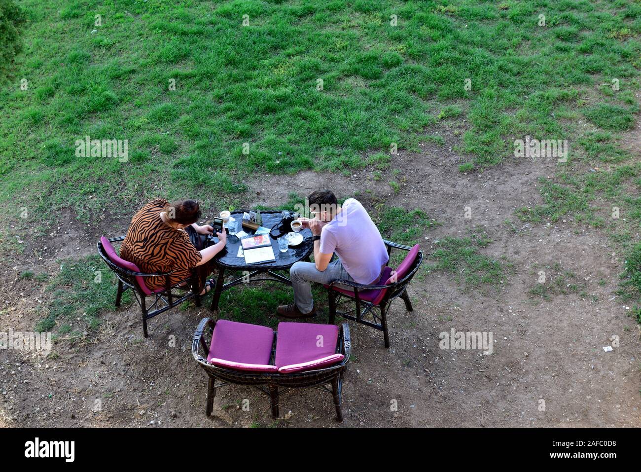 Looking from above at two people eating outside in park at table. She using phone to photograph coffee cup, Rovinj, Croatia Stock Photo