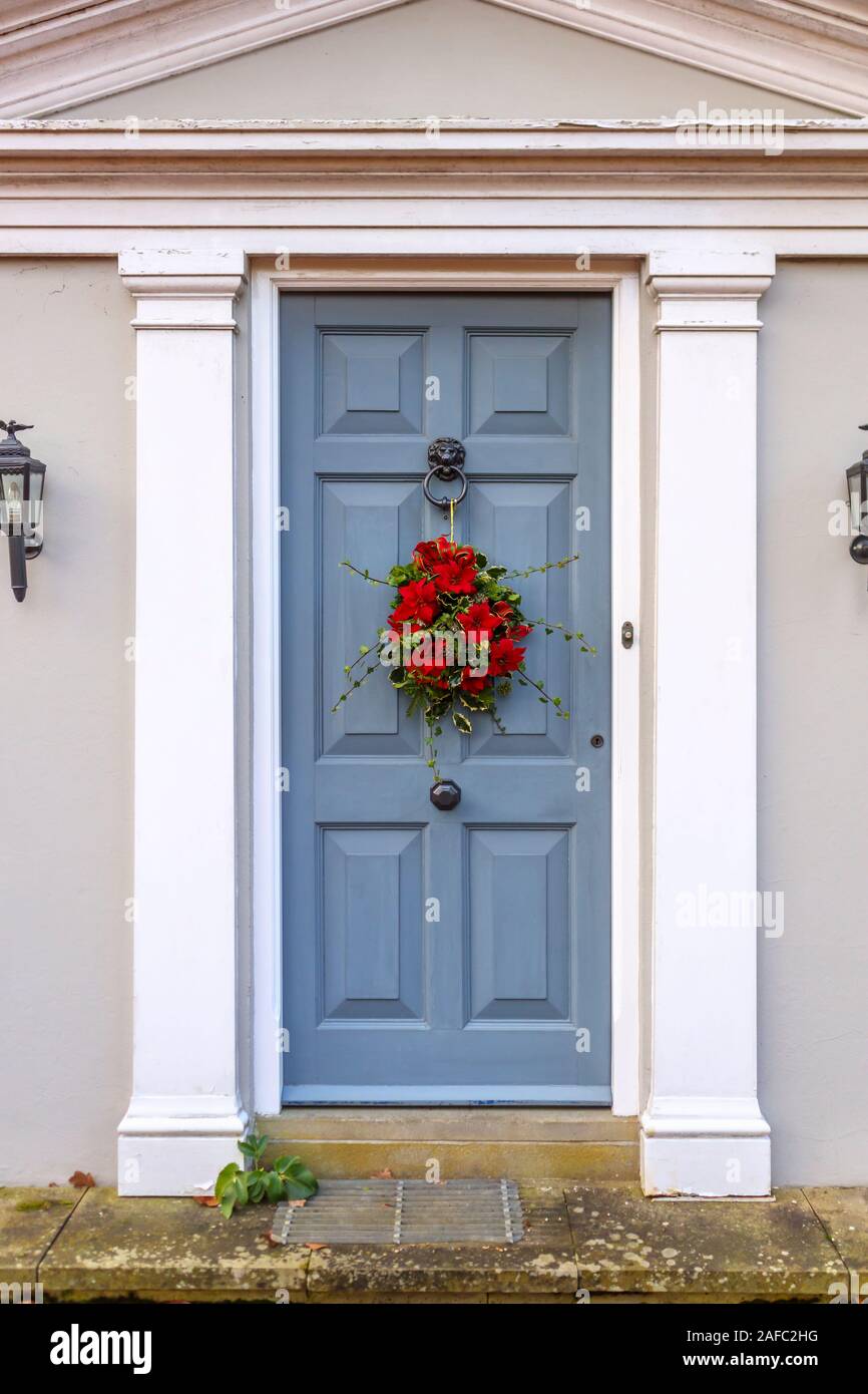 Traditional festive season Christmas wreath arrangement with red flowers and green foliage hanging in a grey front door at a house in Surrey, England Stock Photo