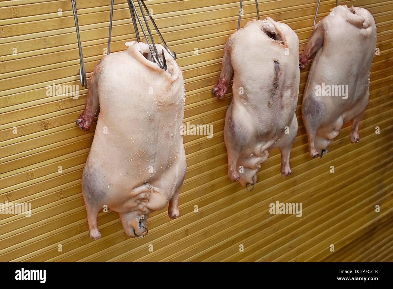 Three stuffed geese before grill hang on steel hooks against a yellow wooden wall Stock Photo