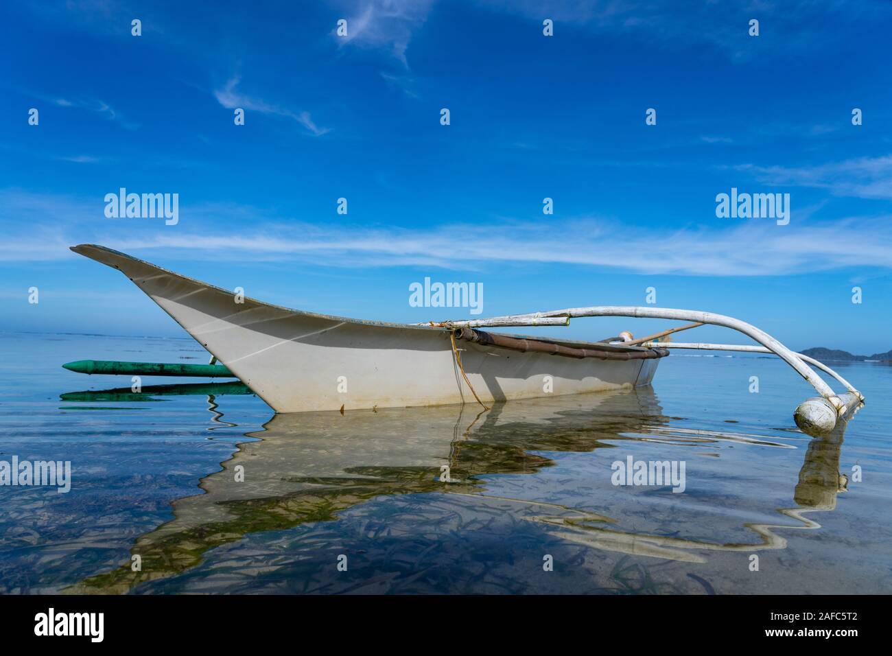 A small outrigger boat known as a Banca in the Philippines moored in calm shallow water. Stock Photo