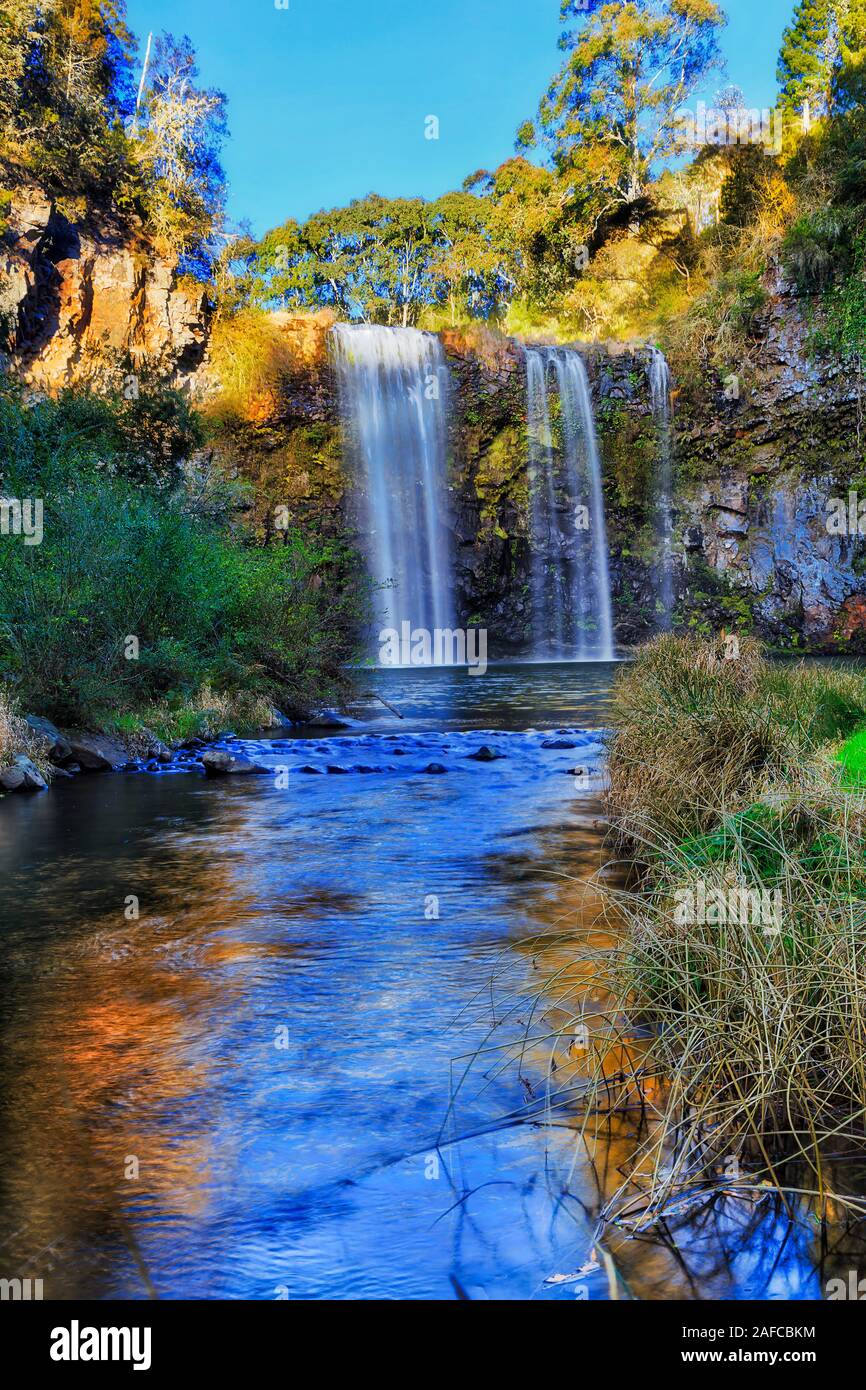 Dandar falls waterfall in Dorrigo national park cutting through lava rocks plateau in soft morning light down water stream between frosty grass. Stock Photo