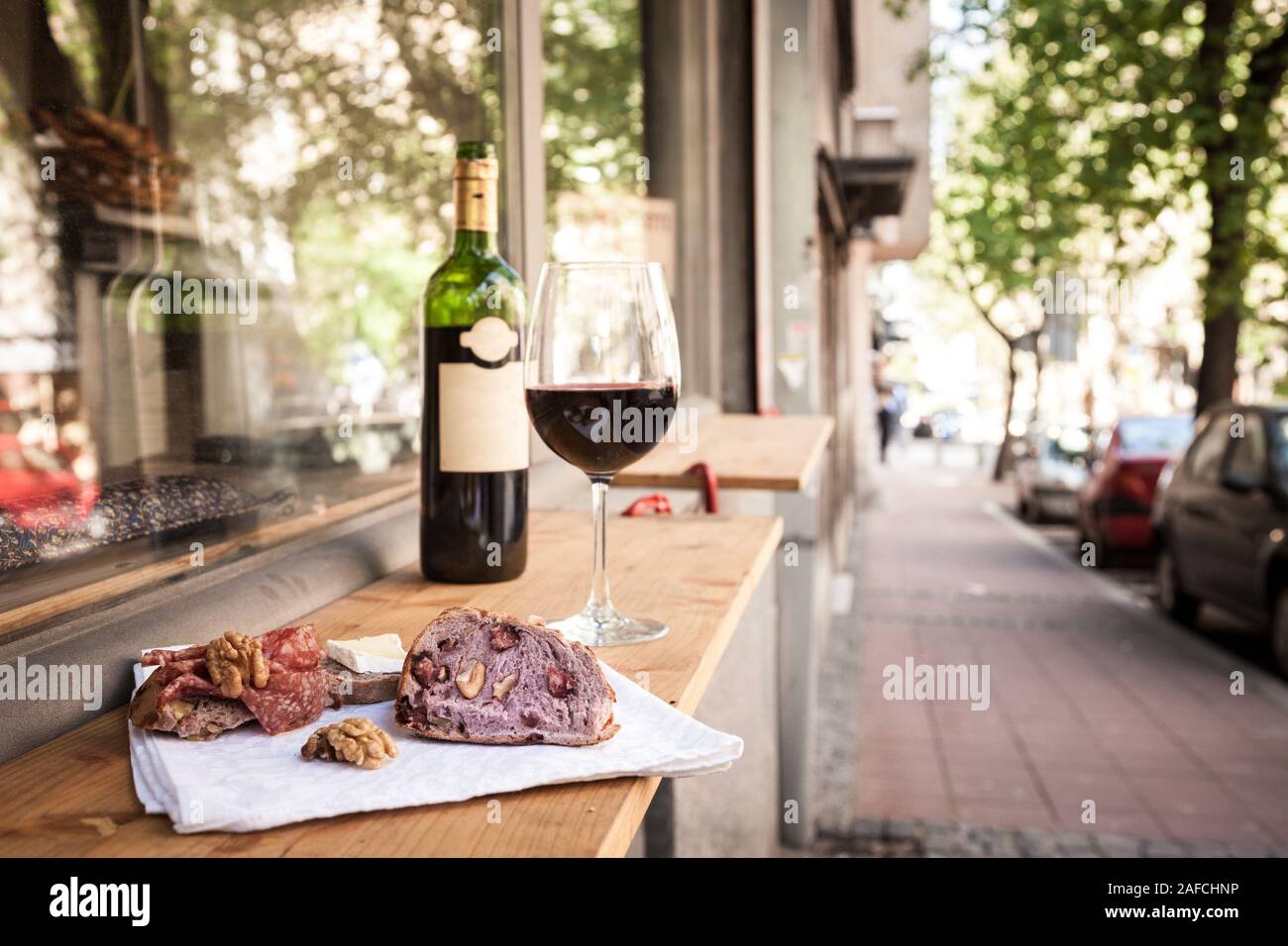 Glass and bottle of French red wine on display on the table of a terrace of Paris with slices of baguette bread, brie cheese and saucisson (a cured me Stock Photo