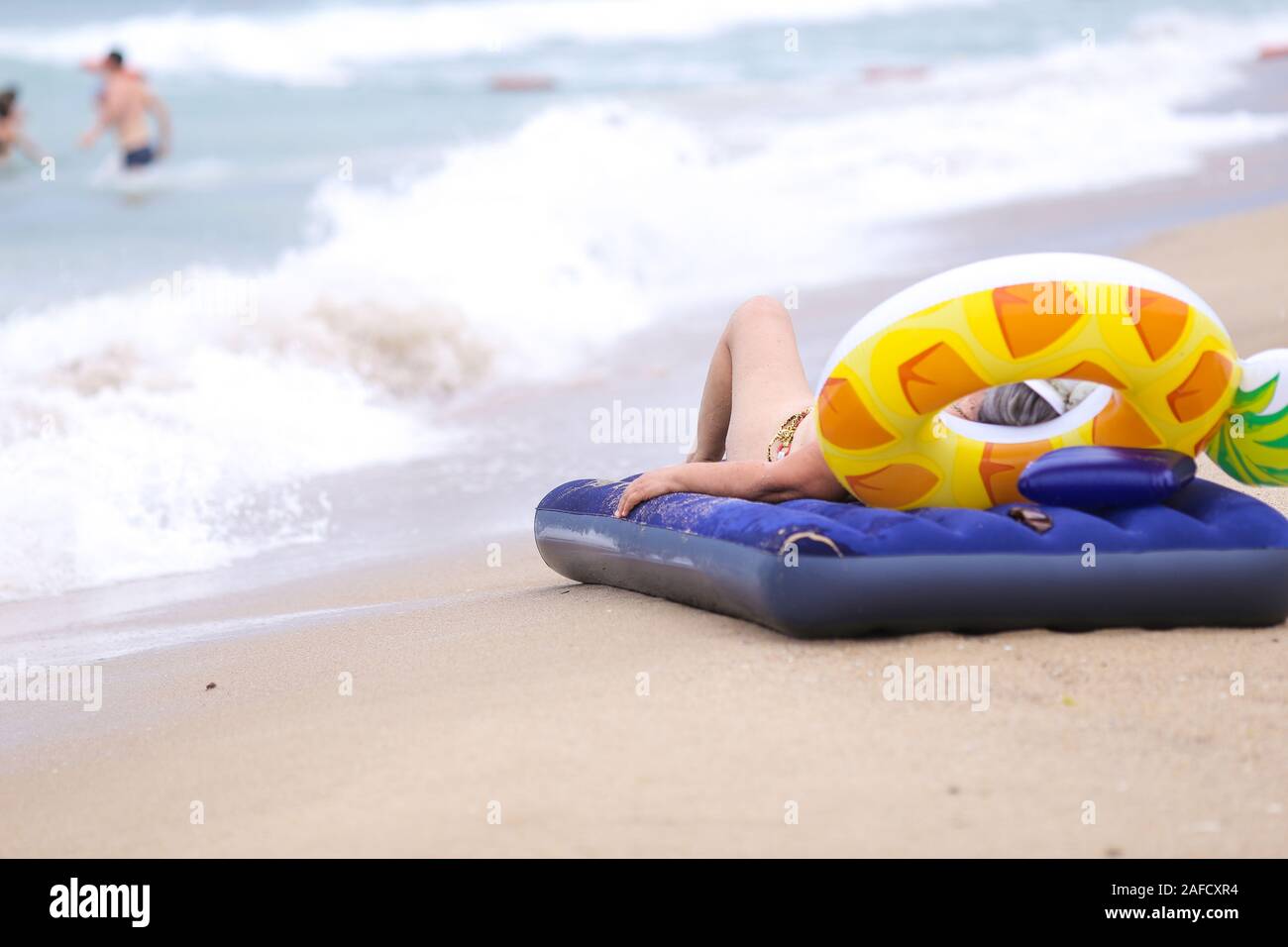 Elderly woman resting on an inflatable mattress on the beach near the water Stock Photo